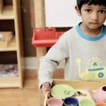young boy carrying tray with play tea set on it